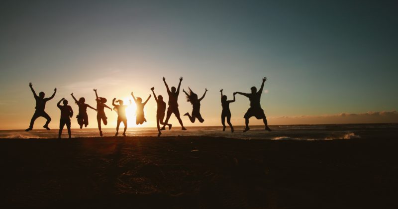A group of people jumping during the sunset at the beach.