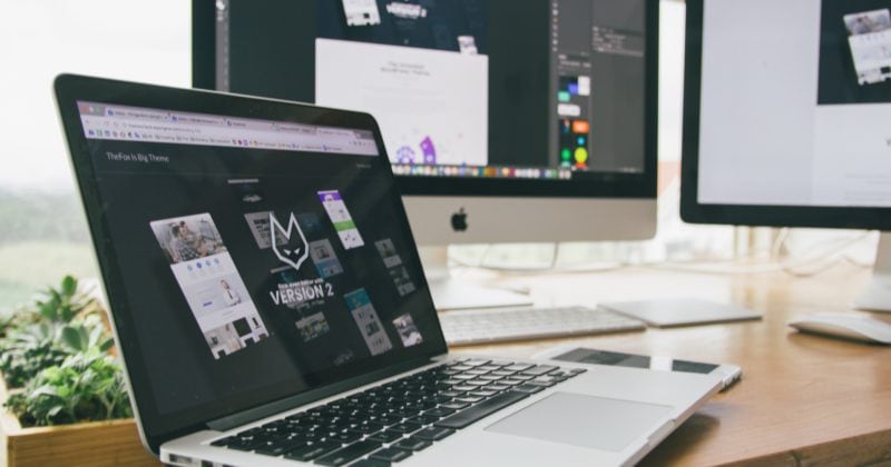 A laptop on a desk with two monitors.