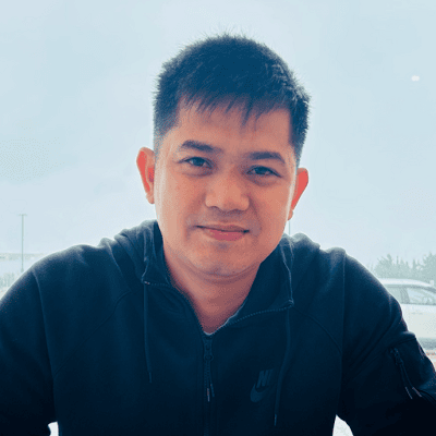 A man in a black Nike jacket sits indoors, smiling softly at the camera. The background shows a foggy window with blurred cars and trees outside.