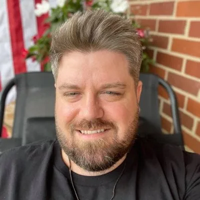 A bearded man named Warren smiling in front of an American flag.