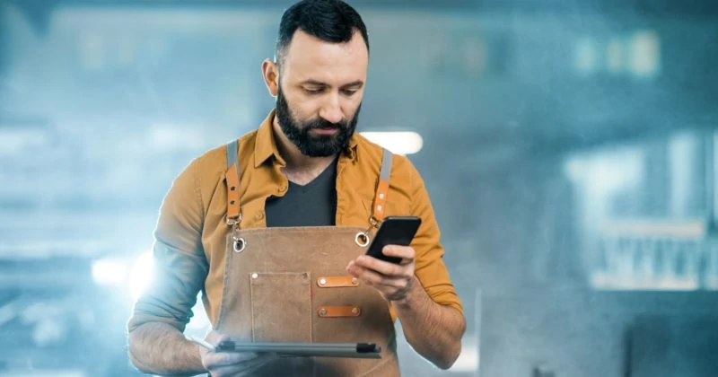 A man in an apron is using a cell phone in a tech-savvy factory.