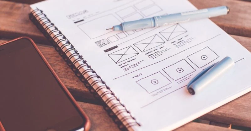 A notebook and cell phone on a wooden table showcasing UI Design's definition.