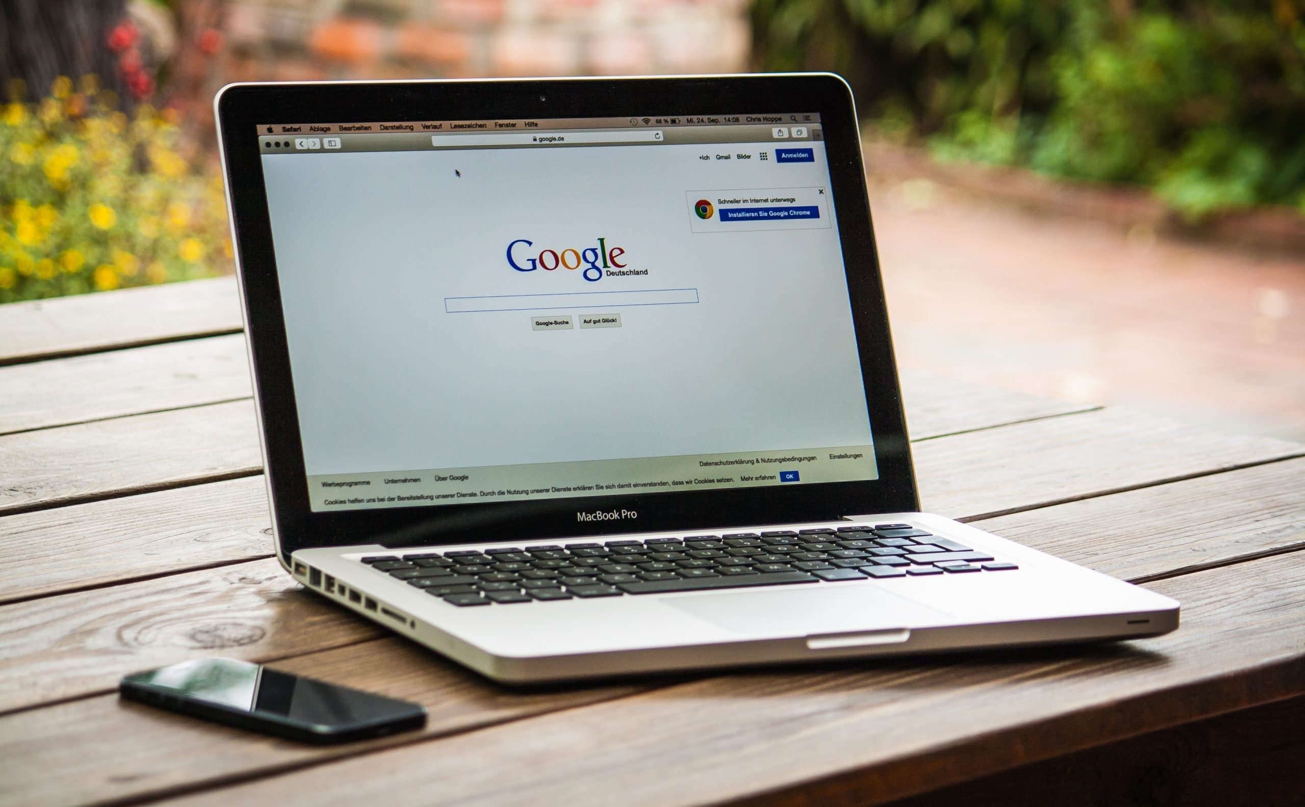 A laptop is sitting on a wooden table next to a cell phone.