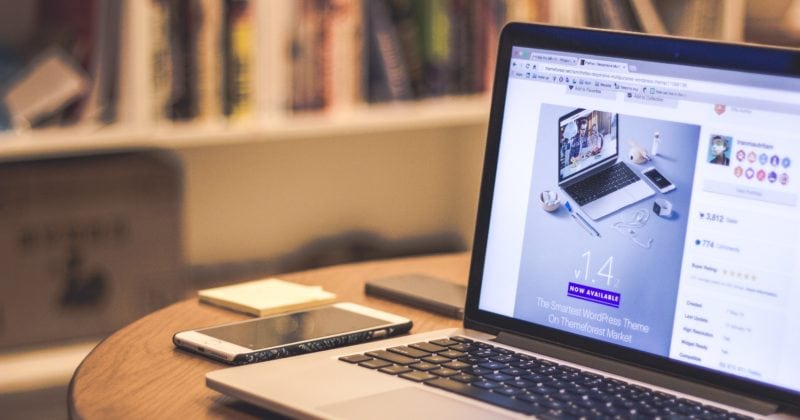 A laptop is placed on a wooden table for SEO and pricing comparison between WIX and WordPress.