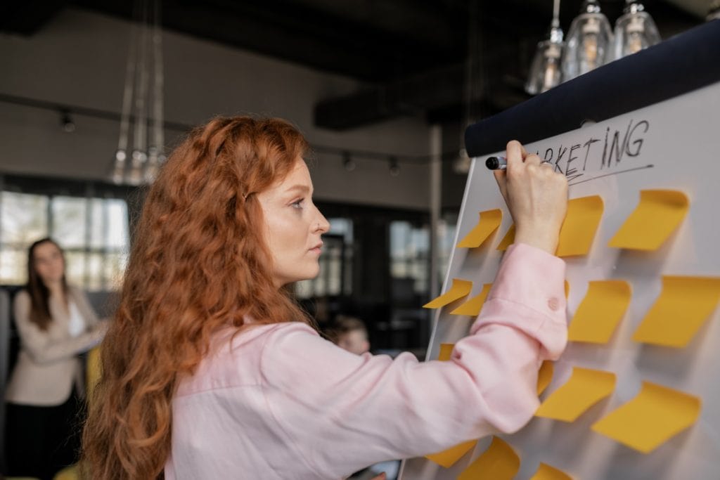 A woman using sticky notes on a whiteboard to plan architectural designs.