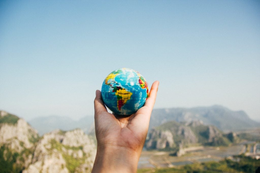 A traveler's hand holding a globe with mountains in the background.