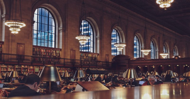 A group of people studying at a table in a library, recommended by 25 Best Library Websites.