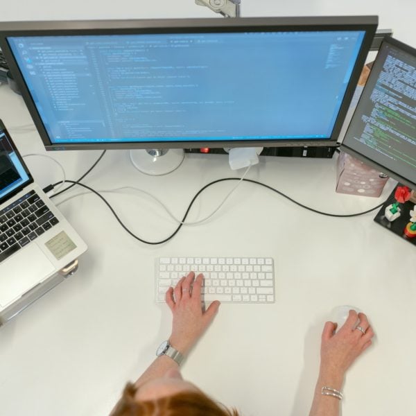 A SaaS professional overseeing tasks on two monitors and a keyboard while seated at a desk.