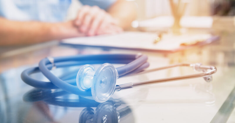 A doctor with a stethoscope in front of a table.