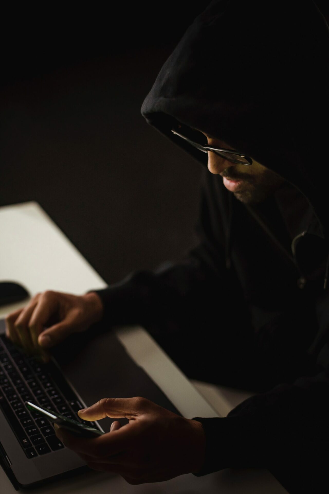 A man in a hoodie is using a laptop computer to exploit the threat of Pwned Passwords.