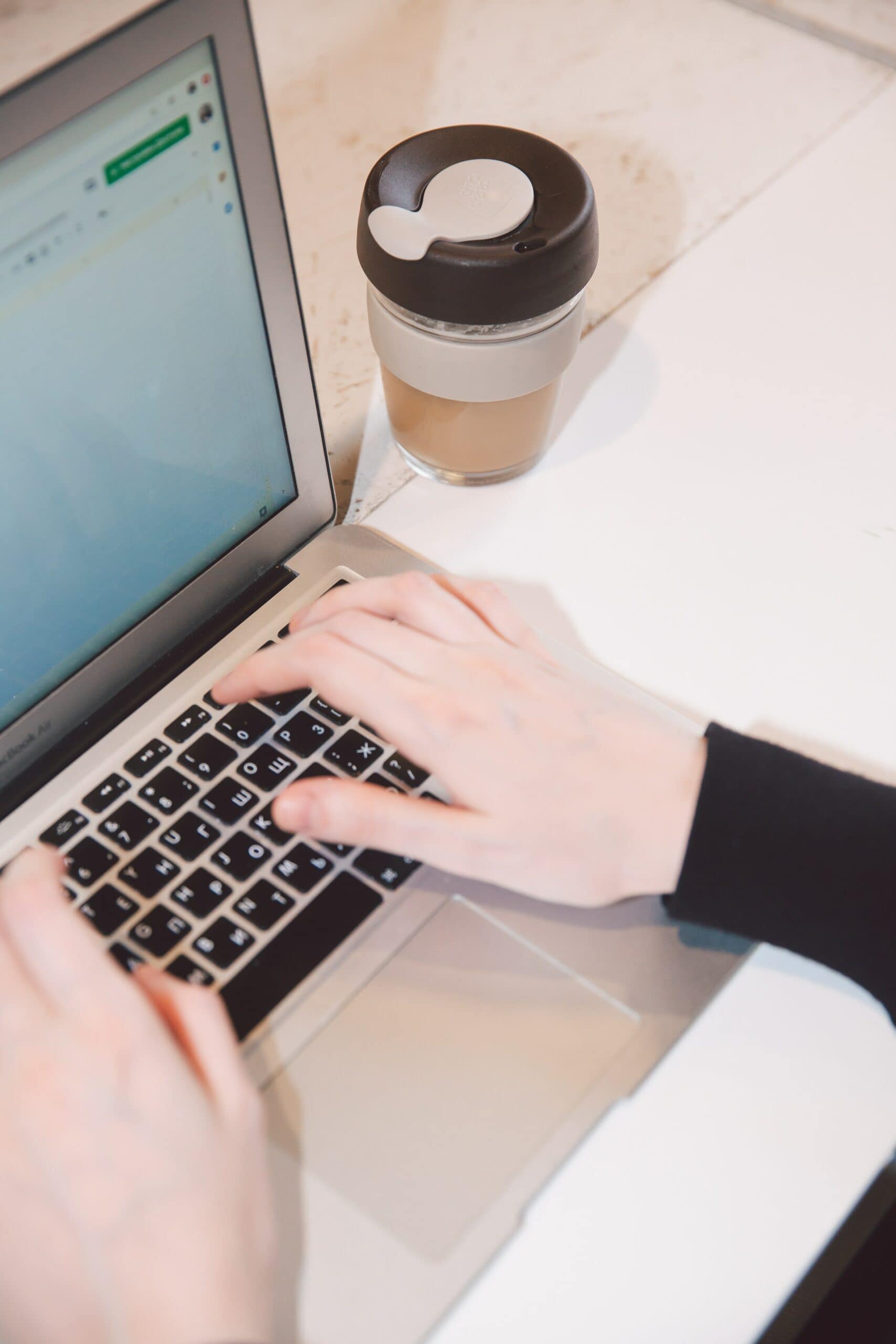 A woman using a laptop to write engaging content with a cup of coffee.