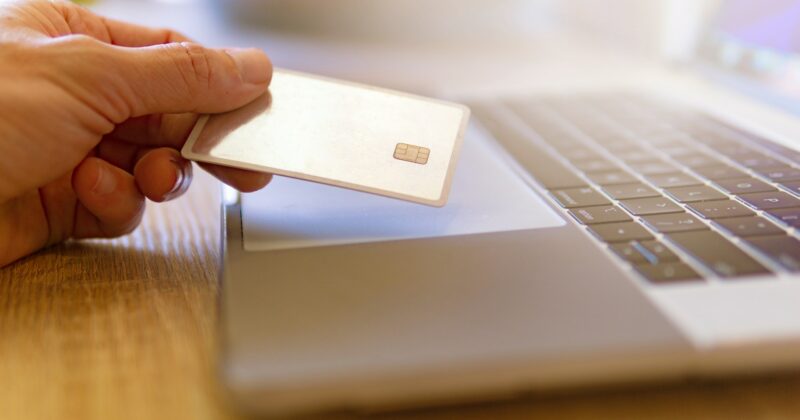 A person is holding a credit card in front of a laptop, symbolizing the threat of pwned passwords.