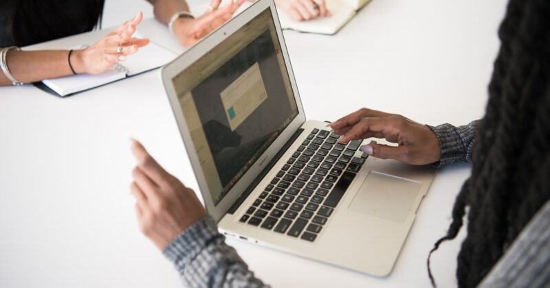 A group of IT professionals utilizing one of the 23 best websites for their work while gathered around a table.