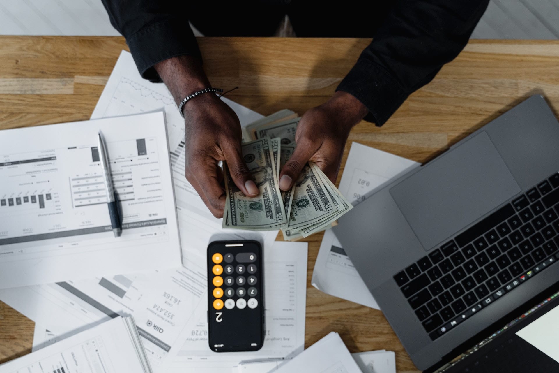 A man holds money and a remote control while sitting at a desk, illustrating the potential vulnerabilities of websites and how they can be hacked.