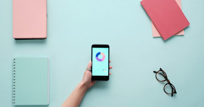 A woman's hand holding a smart phone and a notebook to check page load speed on a blue background.