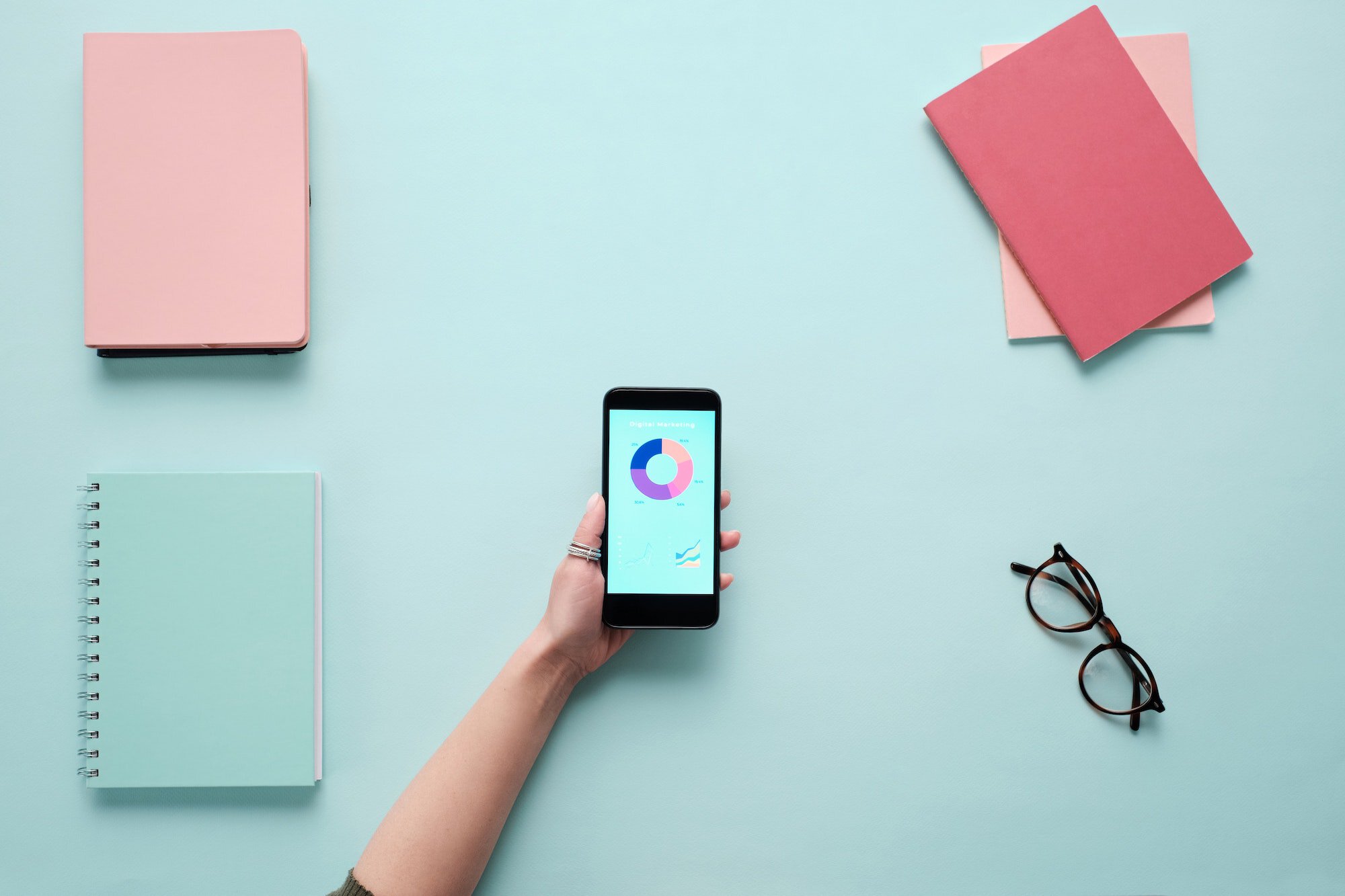 A woman's hand holding a smart phone and a notebook to check page load speed on a blue background.