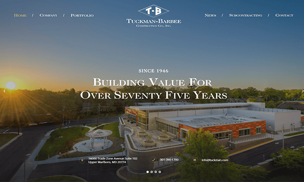 Aerial view of a modern commercial building at sunset, with the Tuckman-Barbee Construction Co. logo and contact info featured on their homepage—an example of standout construction website design.