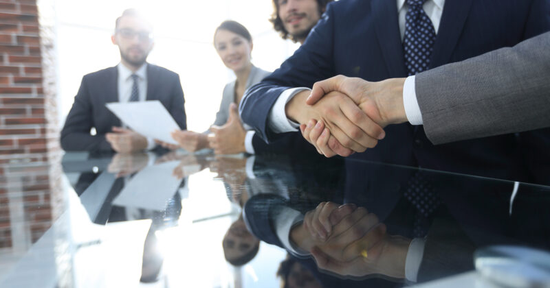 A group of business people shaking hands in front of a glass table at a professional services event.