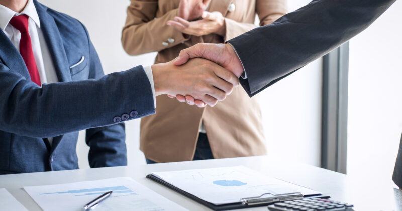 Two business people shaking hands in front of a desk at one of the 22 best recruiters websites.