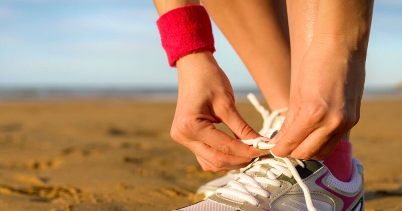 A woman tying her shoes on the beach, captured by a talented photographer.