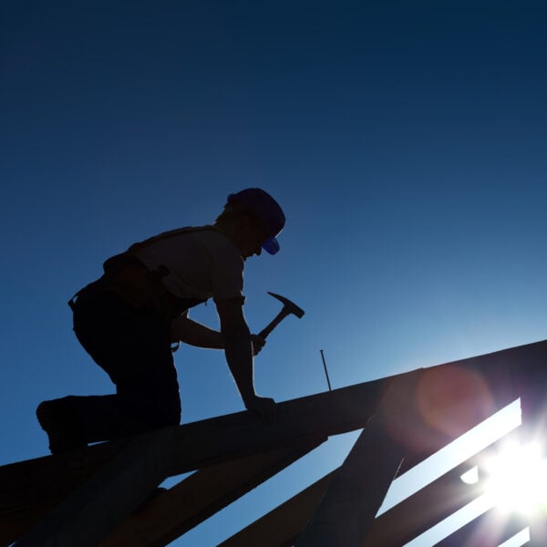 A roofing man with a hammer on a roof.