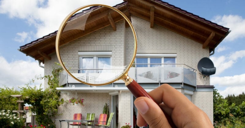 A person holding a magnifying glass in front of a house for the Best Home Inspection Website Designs.