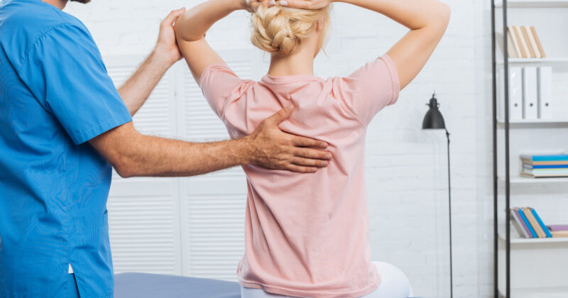 A woman is visiting a physiotherapist for a back examination as part of her physical therapy regime.