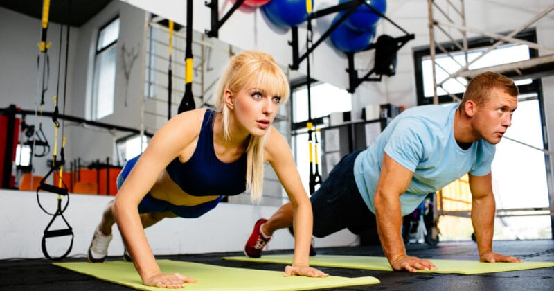 A personal trainer guiding a man and woman through push ups in a gym.