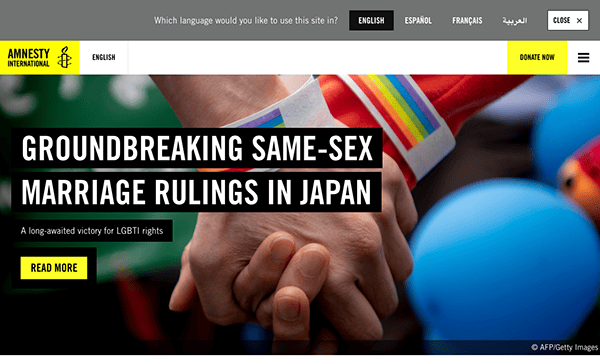 A webpage of amnesty international is featuring a news headline about groundbreaking same-sex marriage rulings in japan, illustrated with an image of two people holding hands with a rainbow wristband.
