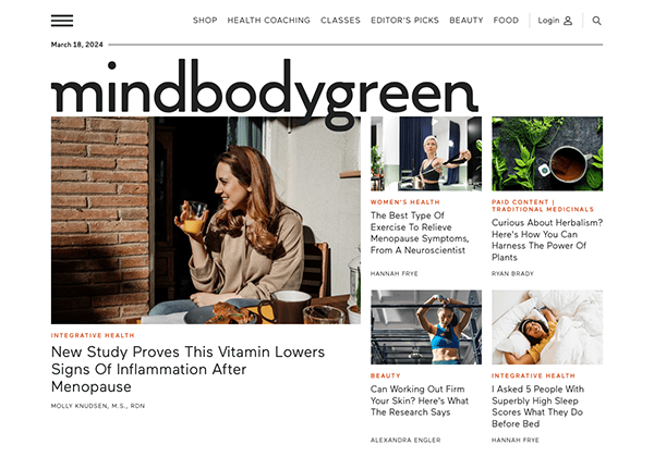 Woman drinking from a cup while browsing through the "mindbodygreen" website on her laptop.