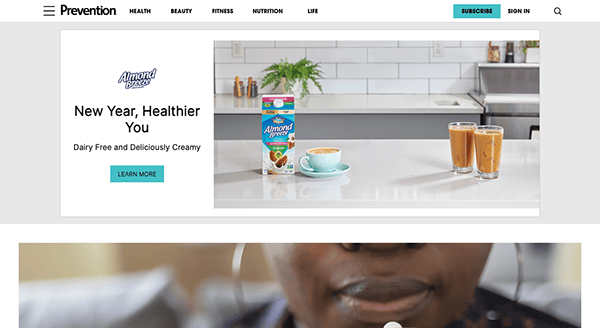 A website homepage with a banner advertisement for dairy-free creamer at the top, featuring a product image and two glasses of beverage, with the navigation menu and partial view of a person's face at the bottom.