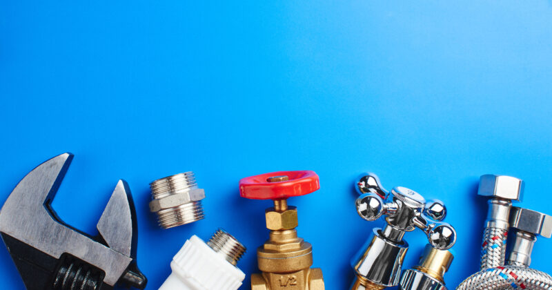 Plumbing tools and parts, including a wrench, pipe fittings, valve, and hose connectors, are thoughtfully arranged on a blue background. This layout not only highlights essential plumbing components but could also inspire innovative website designs with its clean aesthetic.
