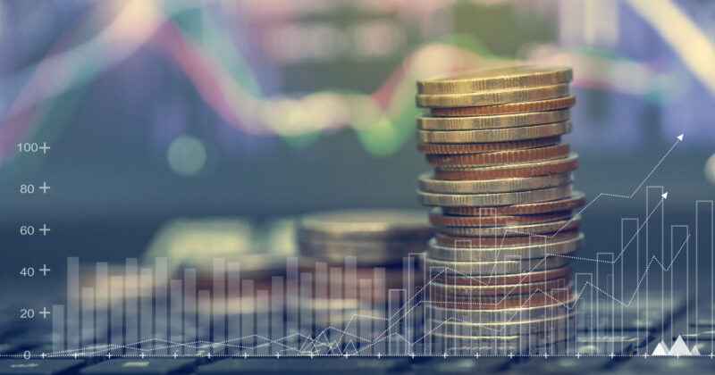 Stack of coins on a desk with private equity financial graphs displayed in the background.