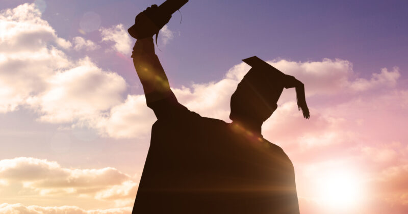 Silhouette of a graduate holding a diploma aloft against a sunset sky, conveying a sense of achievement and celebration in higher education.