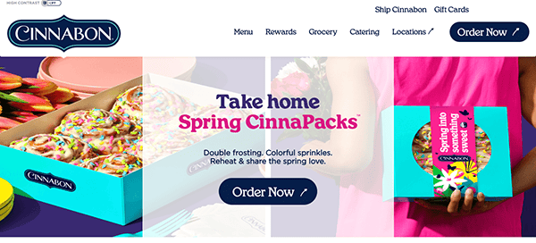 Website homepage of cinnabon featuring an advertisement for spring cinnapacks with a smiling woman holding a box of colorful, frosted cinnamon rolls.