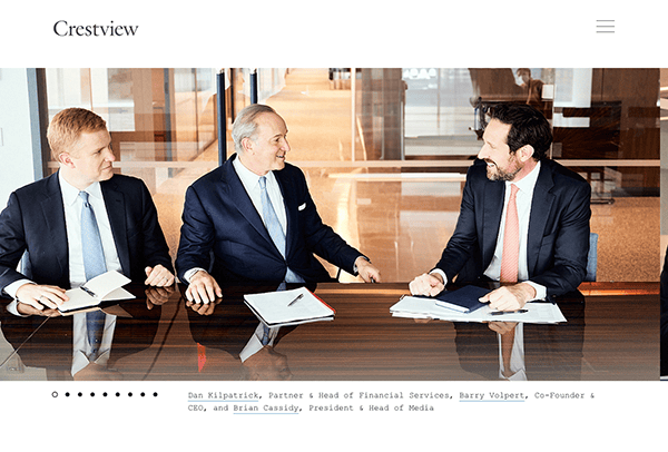 Three businessmen in suits engaged in a discussion at a table with documents in an office setting.