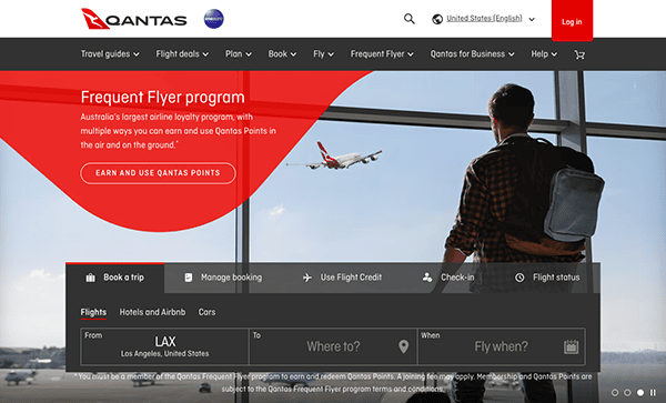 Man at an airport, sitting and looking at a runway through a window while browsing the qantas frequent flyer program on a laptop.
