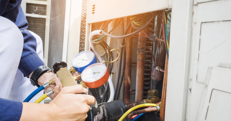 Technician using manifold gauge to check and service an HVAC unit.