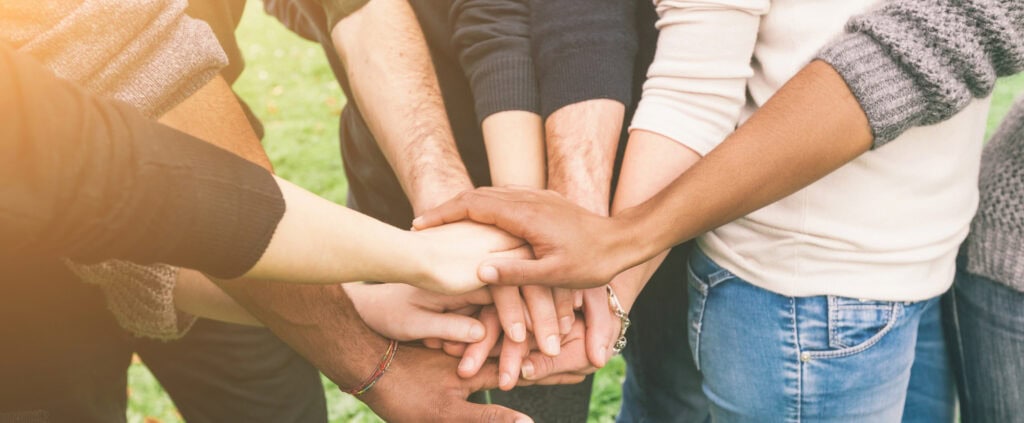 A group of therapists standing in a circle with their hands stacked in the center, symbolizing unity and teamwork.