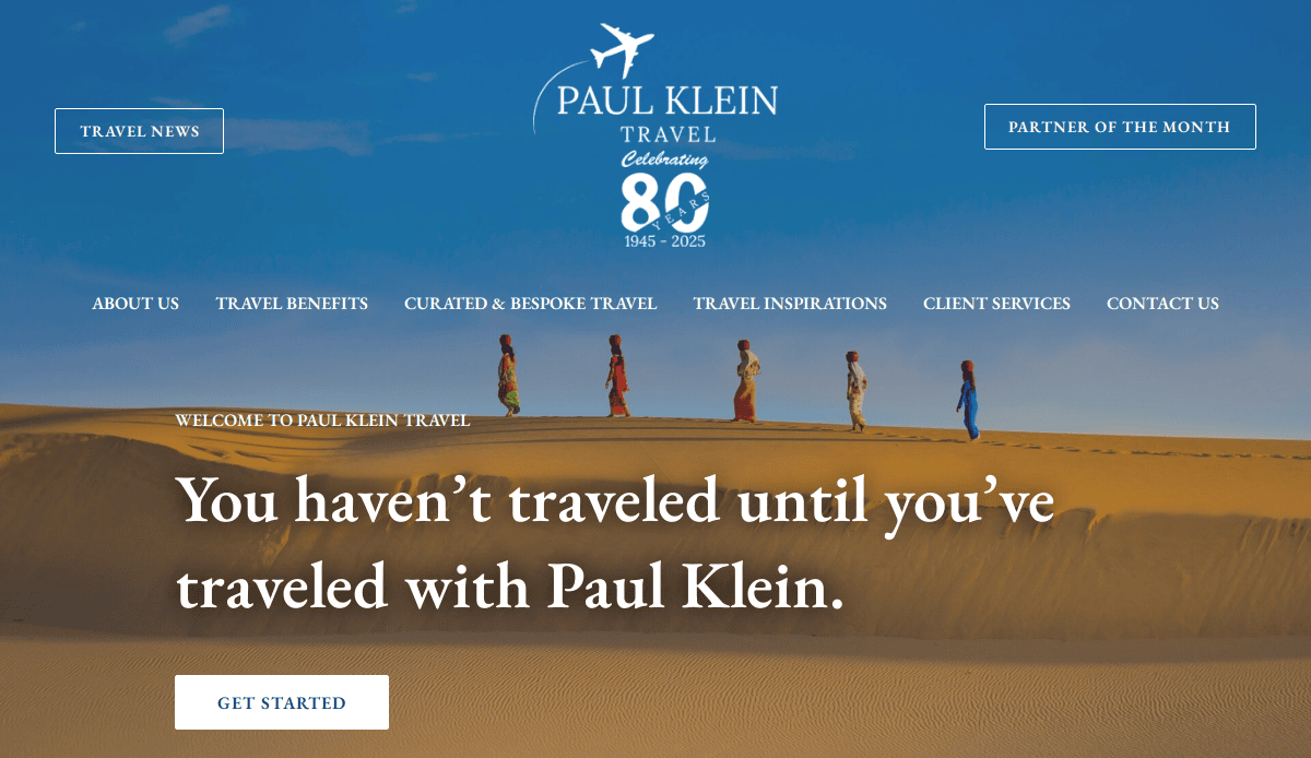 A desert scene with five people walking on sand dunes under a blue sky. Text reads: You haven’t traveled until you’ve traveled with Paul Klein. Explore our tourism website, navigation links, and 80th anniversary logo at the top.
