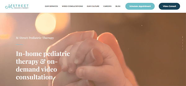 Close-up of an adult hand holding a child's hand, with text overlay promoting in-home pediatric therapy and on-demand video consultations for M Street Pediatric Therapy.