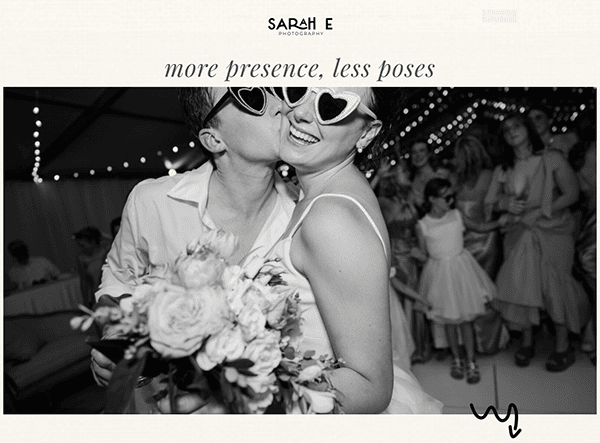A couple wearing heart-shaped sunglasses smiles and embraces at a wedding reception, bouquet in hand and guests dancing in the background—a perfect moment for any photography portfolio or photographer websites.