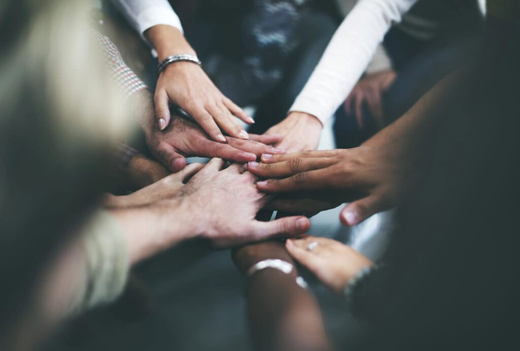 A group of people places their hands together in the center, showcasing unity and teamwork, demonstrating a commitment to ADA Compliance.