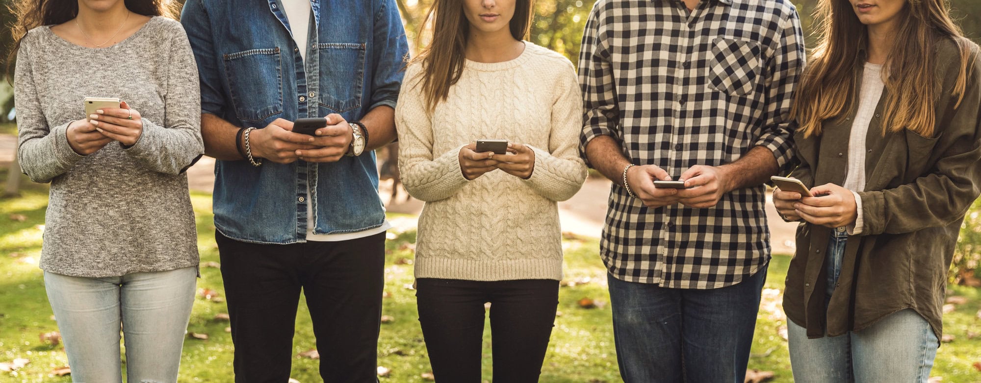 Five people standing in a row outside, looking down at their smartphones, likely using a posting service or browsing social media. They are dressed in casual clothing, and their faces are not visible.