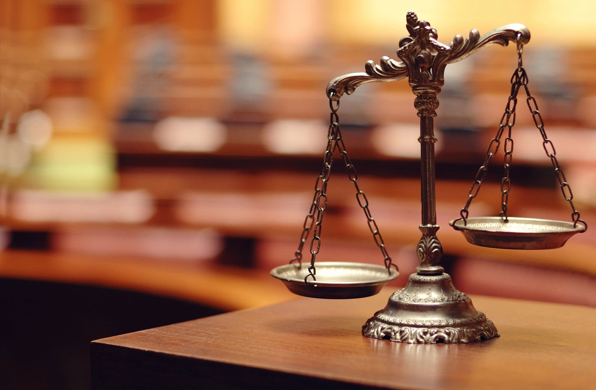 A bronze balance scale is placed on a wooden desk in a blurred courtroom setting, symbolizing the careful consideration of data protection policies.
