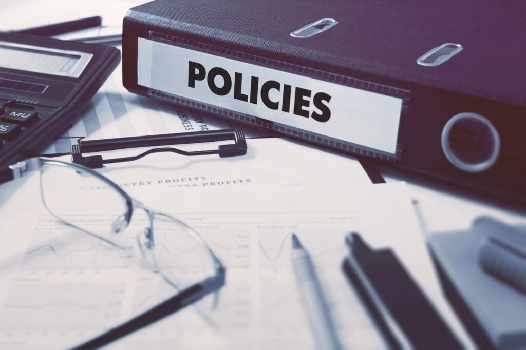 A binder labeled "POLICIES" rests on documents with graphs, next to a calculator, glasses, and pens, ensuring a clear view of privacy considerations.