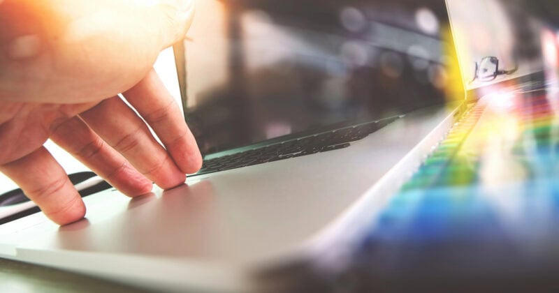 A hand reaches towards a laptop keyboard, with sunlight reflecting off the screen and creating colorful lens flares. It's a glimpse into the web design trends that small businesses are embracing for 2025.