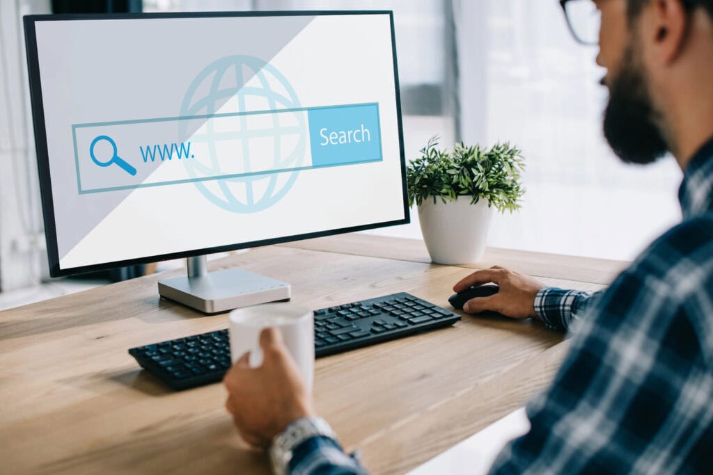A man uses a computer, the screen showing a Google Local Service Ads search bar. A plant sits quietly on the desk, adding a touch of nature to his Ads Management workspace. 