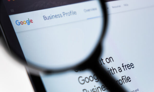 A magnifying glass focuses on a computer screen displaying the Google Business Profile webpage, highlighting its various categories to optimize business visibility.