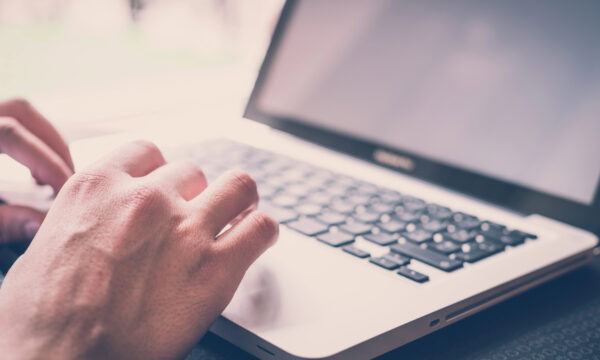 A person types on a laptop with a black keyboard and silver casing, carefully focusing on the left side of the keyboard, highlighting accessibility features.